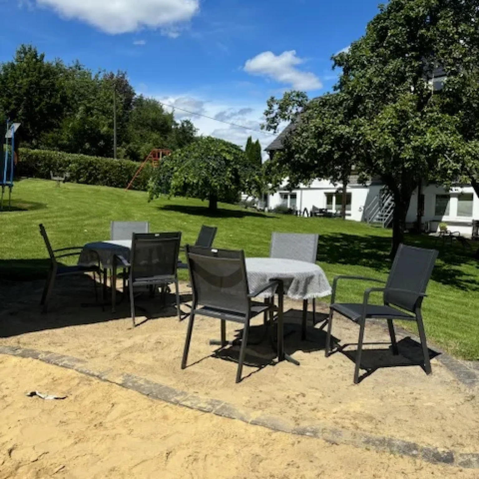Tisch und Stühle aus schwarzem Metall im Freien auf einem Sandboden mit Gras im Hintergrund.