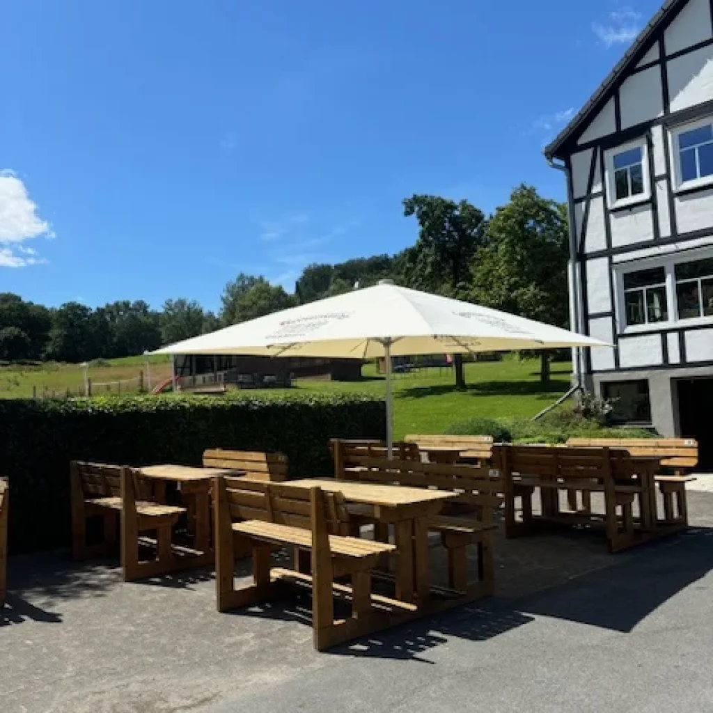 Holztische und Bänke unter einem großen Sonnenschirm auf einem Hof.