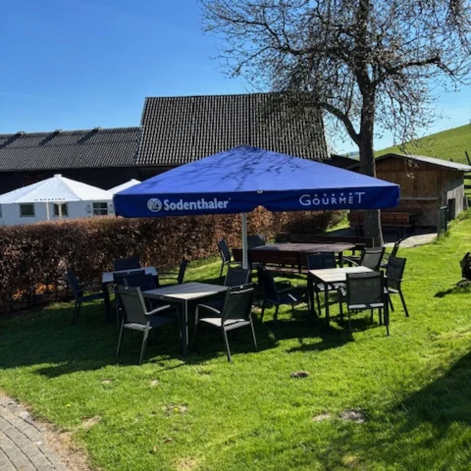 Blauer Pavillon mit dem Logo von Sodenthaler und mehreren Tischen im Gartenbereich.