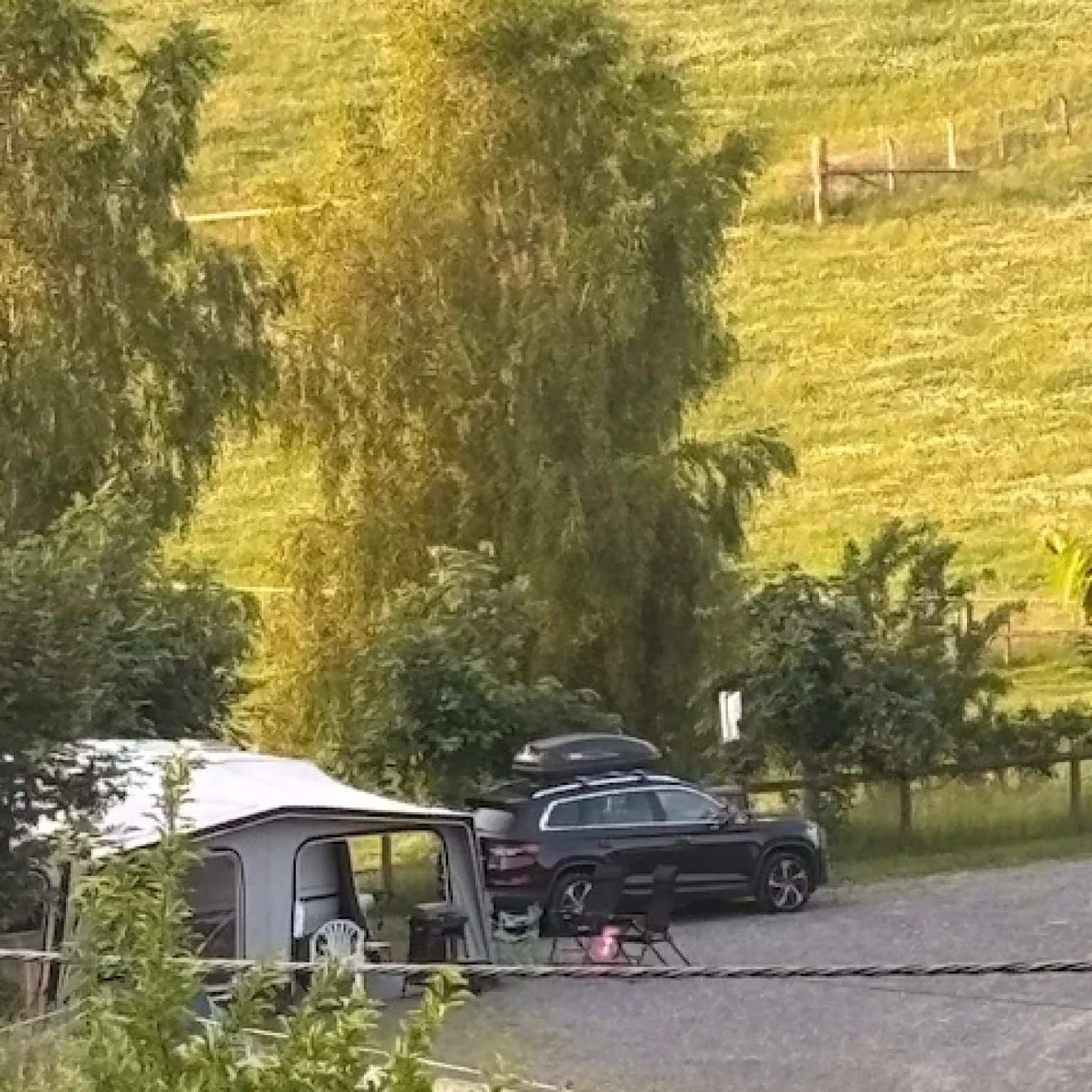 Schwarzes Auto steht neben einem Wohnwagen auf einem Campingplatz mit grüner Wiese im Hintergrund.