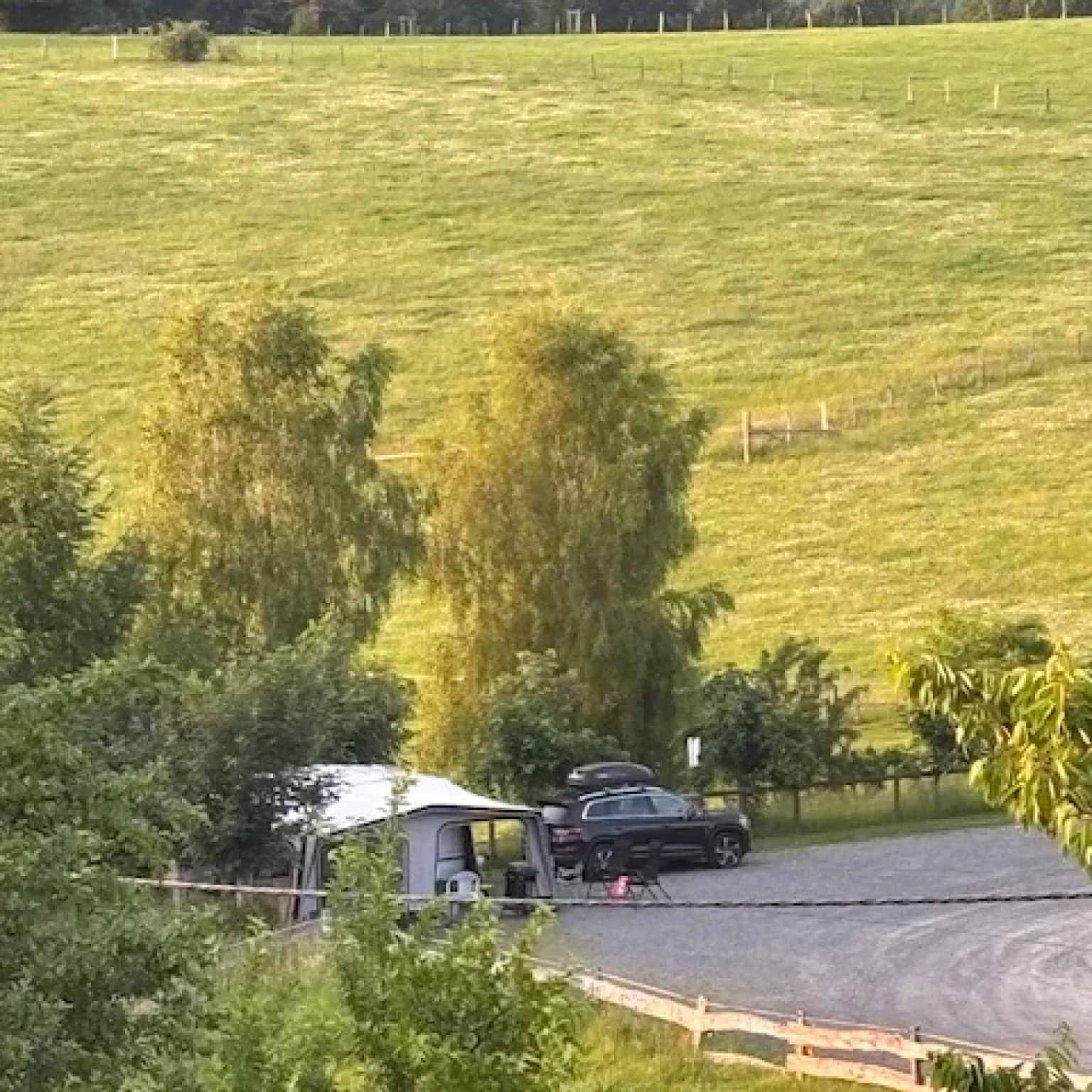 Ein Wohnmobil und ein Auto auf einem Parkplatz in einer ländlichen Umgebung mit Wiese im Hintergrund.